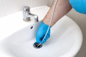 gloved-hand-feeding-drain-snake-into-sink