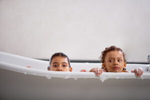 two-kids-peeking-out-of-the-bathtub-with-mischievous-expressions