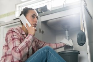 person-with-phone-to-ear-and-cloth-in-hand-under-kitchen-sink